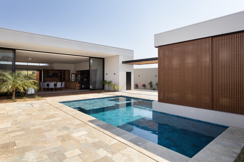 Courtyard pool with perforated timber screen wall, white stucco volumes, and sandstone paving under a clear sky