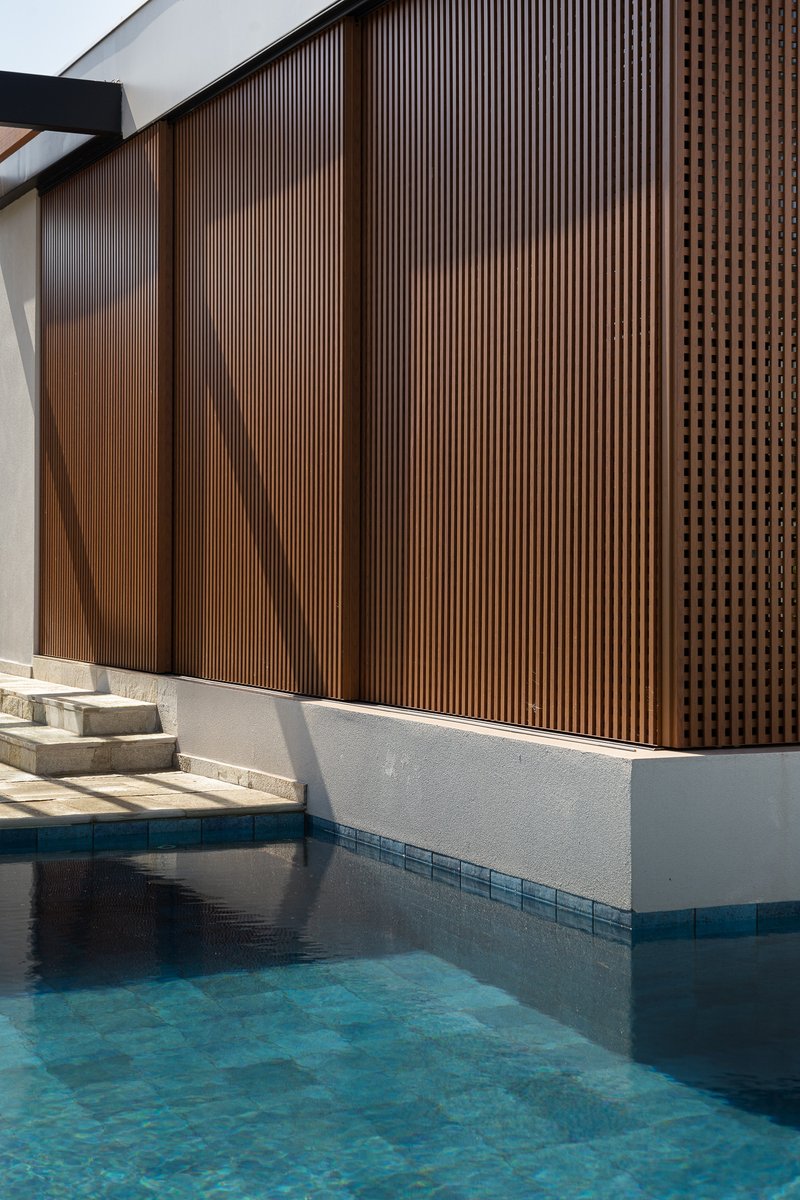 Pool edge detail showing the timber slat screen panels above a white plaster base reflected in the water
