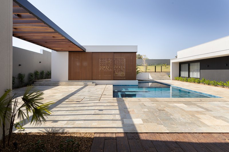 Courtyard view with patterned paving, timber deck inset, pool, slatted screen wall, and cantilevered timber soffit casting shadows