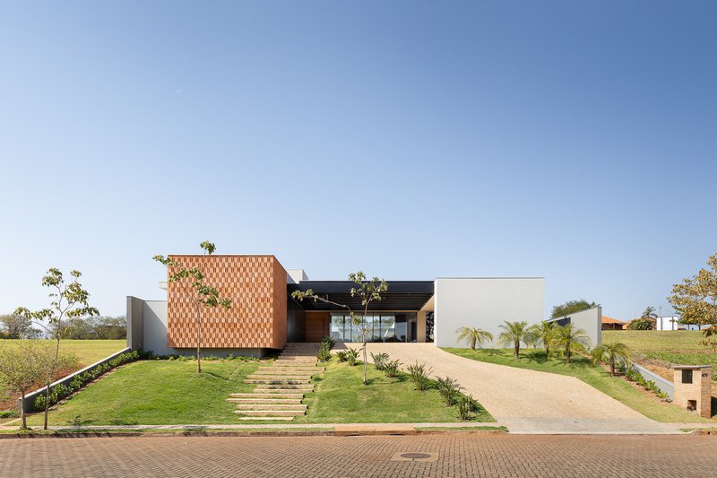 Street view of the residence with patterned terracotta facade volume and young trees under clear blue sky