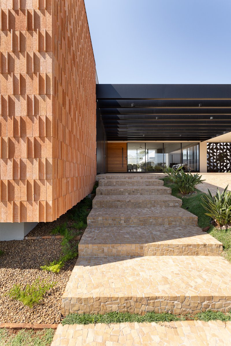 Entry walkway with stacked stone steps ascending past terracotta screen wall and planted agave specimens