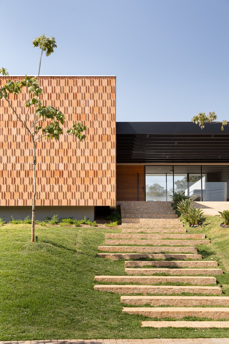 Brick-paved stairway ascending through lawn toward the textured facade and glazed entry