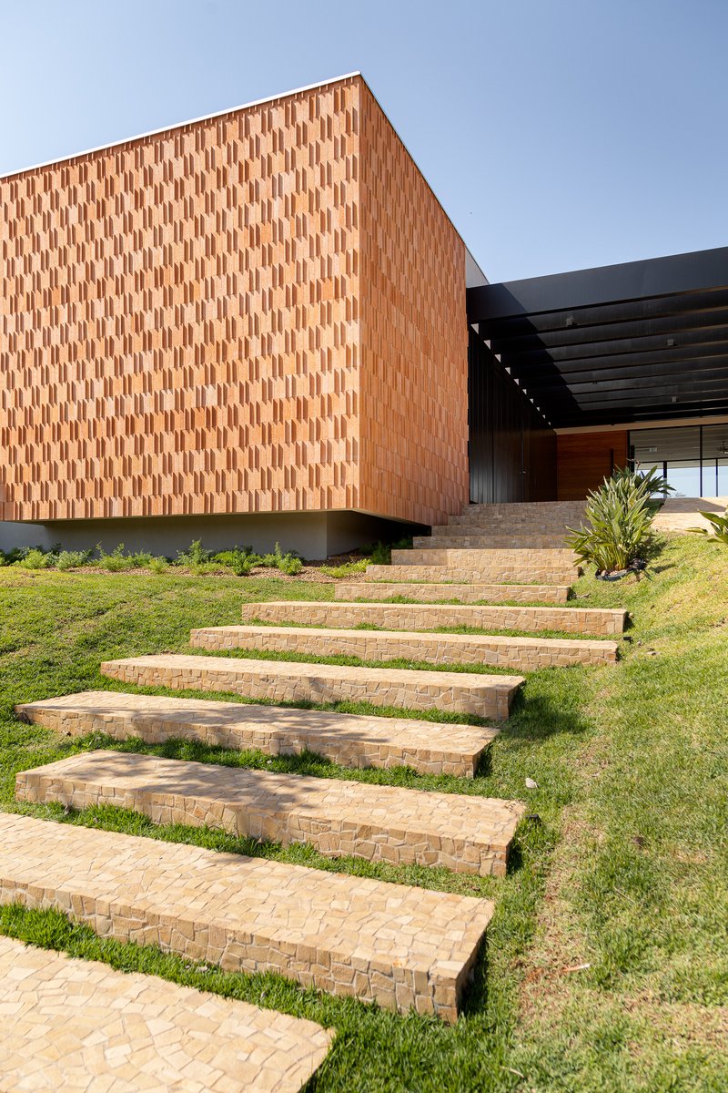 Close view of the brick-paved steps cutting through grass toward the cantilevered brick volume