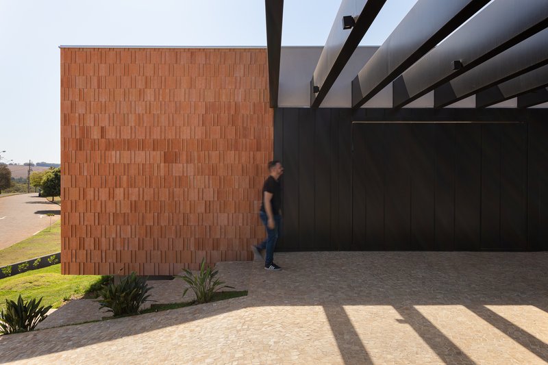 Covered carport with steel pergola beams and a figure walking past the textured brick wall