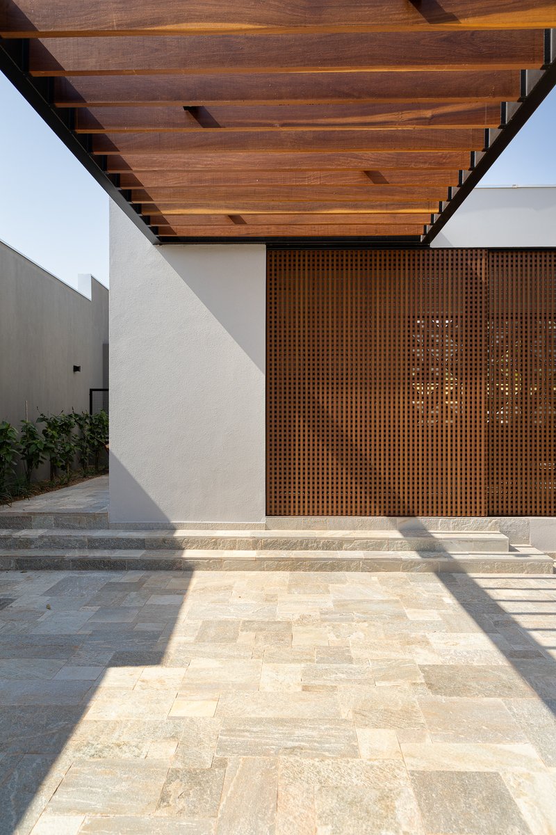 Entry courtyard with perforated timber screen doors beneath exposed timber rafters and afternoon shadows