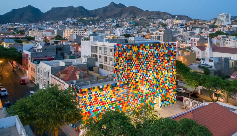 Aerial view of the pixelated polychrome facade rising above surrounding residential buildings at twilight