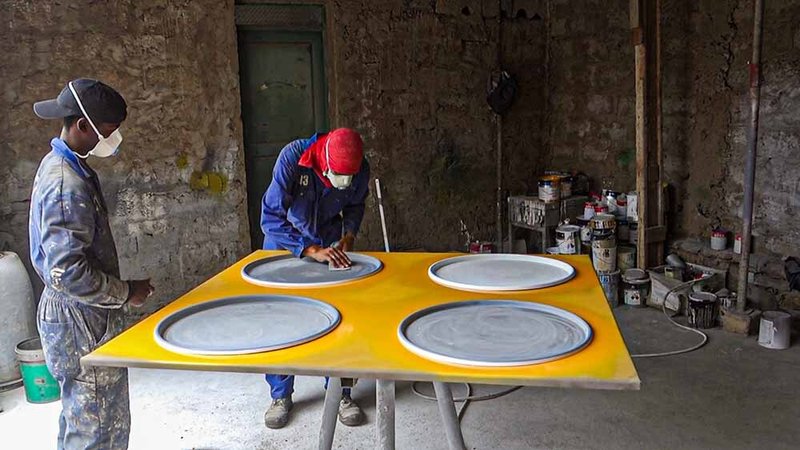 Two workers finishing circular openings in a yellow prefabricated panel in a workshop