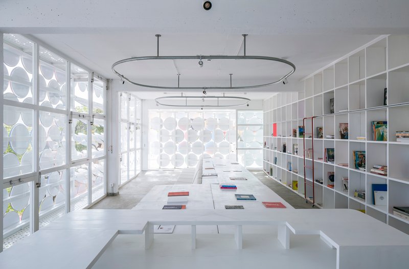 Interior reading room with white shelving, concrete floor, oval ceiling rails and daylight through perforated screens