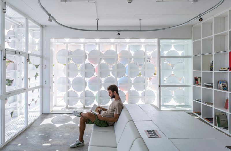 Interior room with circular patterned screen wall casting dappled shadows on a person seated on white platform