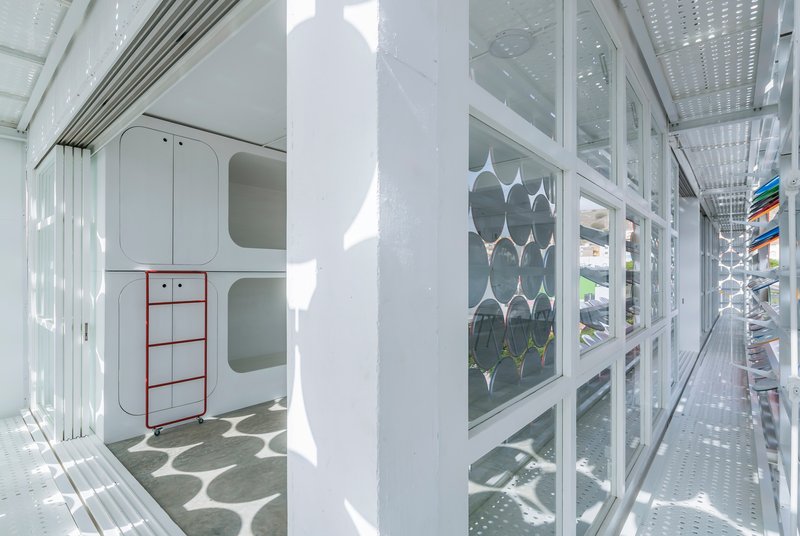 Narrow corridor with perforated metal ceiling and glazed wall overlooking the circular screen facade and plants