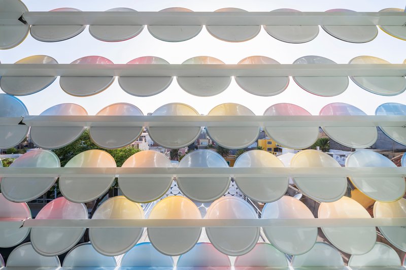 Facade detail showing overlapping translucent circular glass panels in pastel hues on horizontal supports
