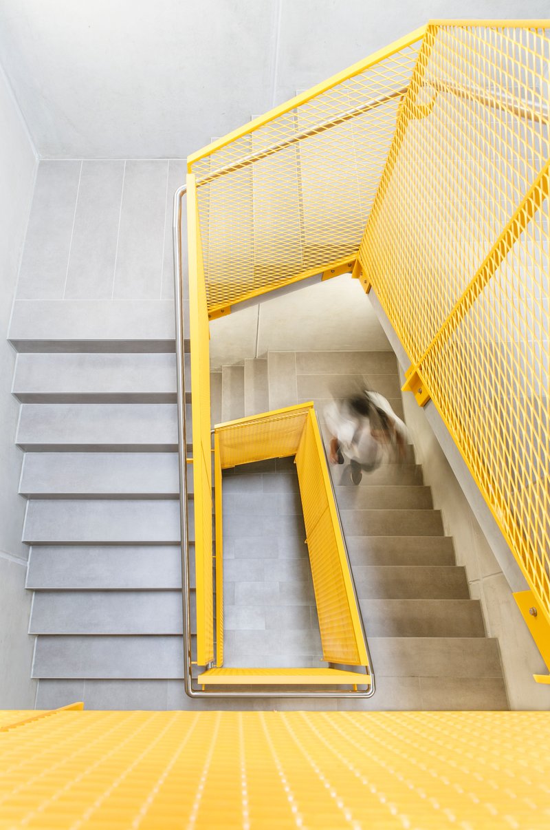 Top-down view of yellow metal mesh stairwell with a person descending the concrete steps