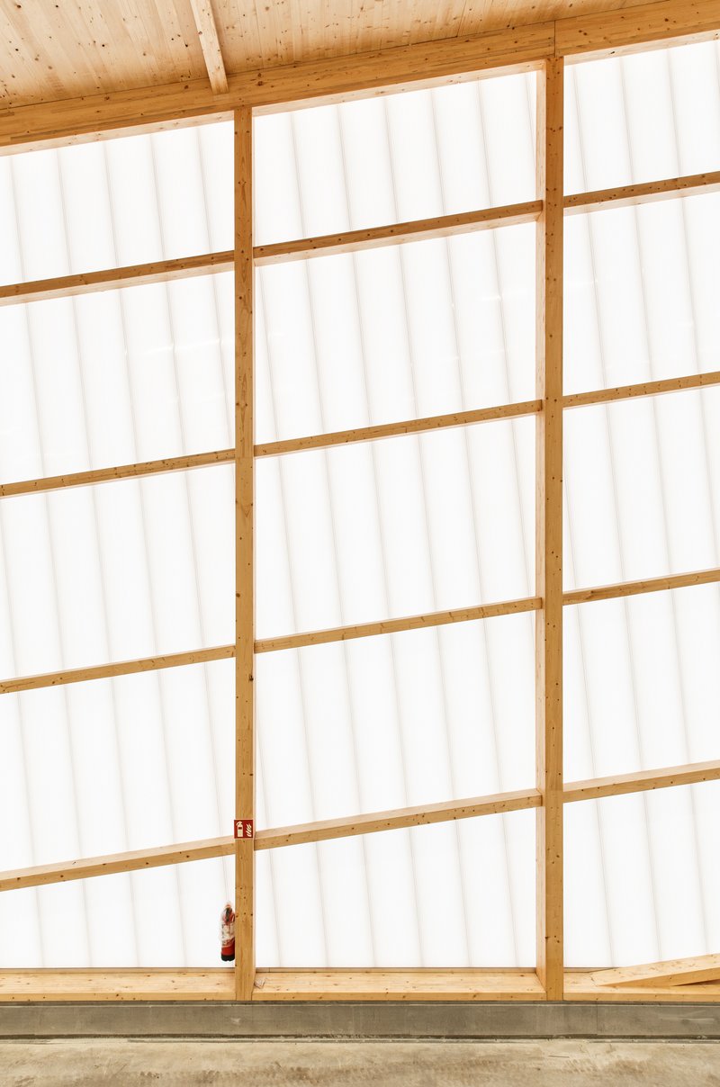 Floor-to-ceiling translucent polycarbonate wall with timber framing and exposed wood beam structure above