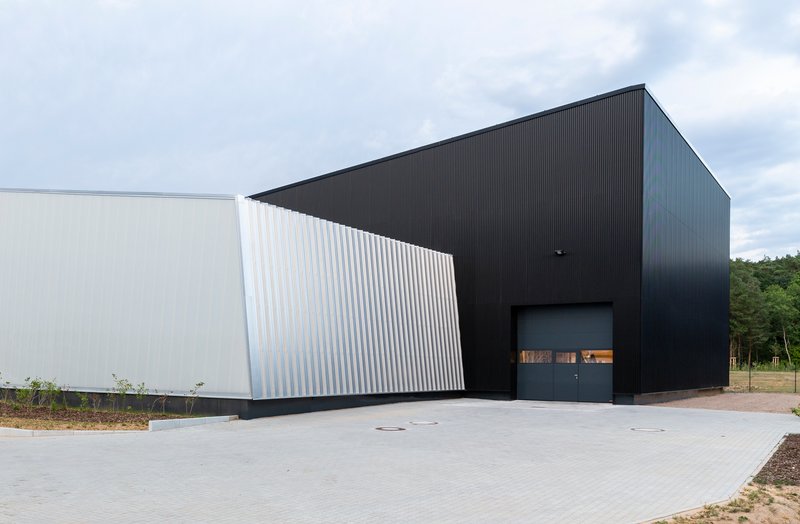 Entrance facade with black corrugated metal cladding and recessed glazed opening on paved forecourt