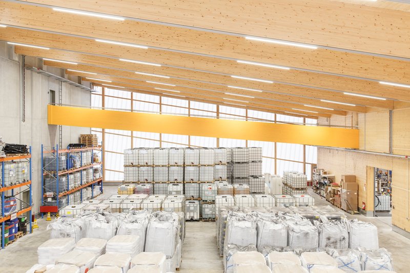 Interior warehouse space with exposed timber ceiling beams, clerestory glazing, and stacked bulk material containers