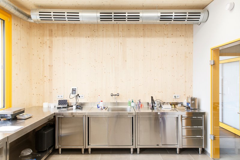 Kitchenette with stainless steel counters beneath cross-laminated timber wall panels and cylindrical ventilation duct