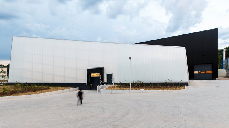 White ribbed facade wall with black framed entrance canopy and figure in motion crossing the pavement