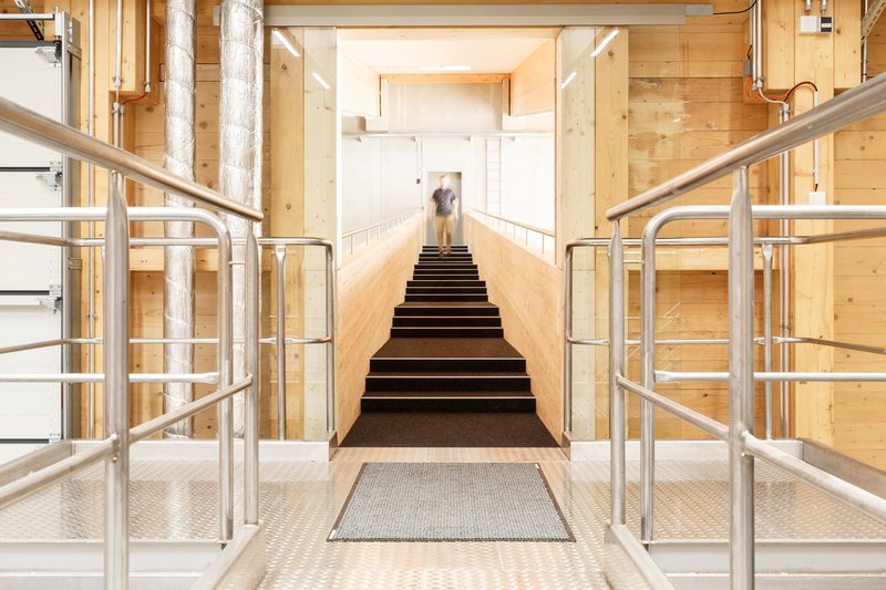 Central stairway flanked by steel railings and exposed timber-lined walls with a person at the landing