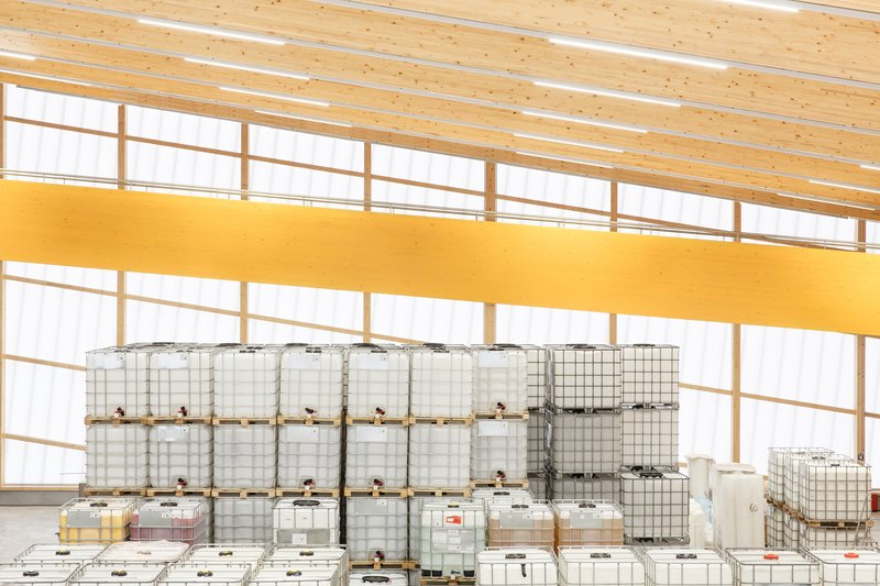 Interior view of industrial storage area with white plastic containers stacked below a yellow mezzanine and timber ceiling