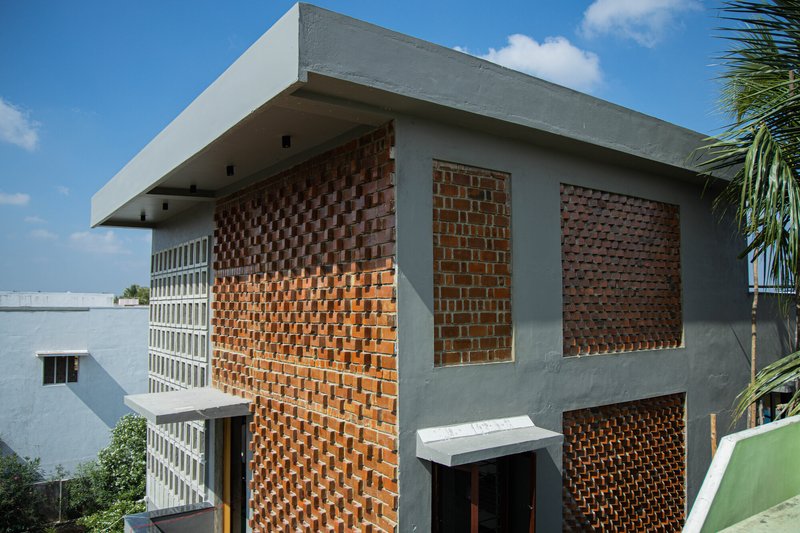 Two-story facade with perforated brick screens and concrete frame under a clear blue sky with palm fronds