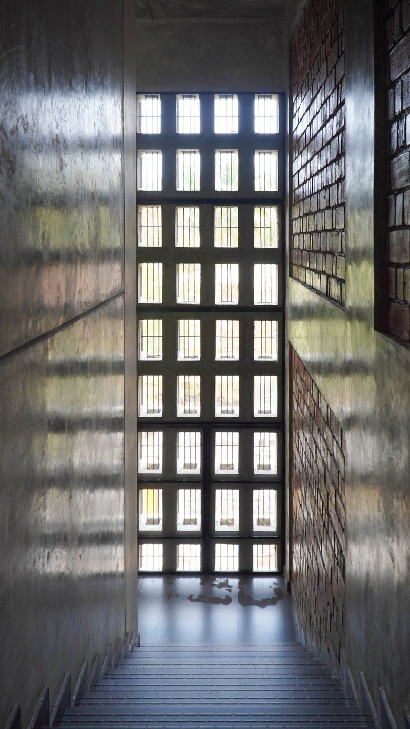 Staircase with gridded window wall casting shadows on concrete side walls and brick screen
