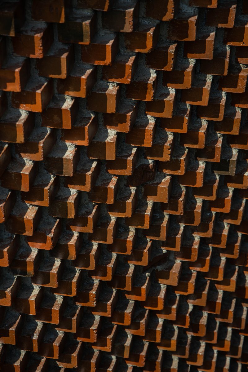Close-up of projecting terracotta bricks in a stepped diagonal pattern creating shadow play