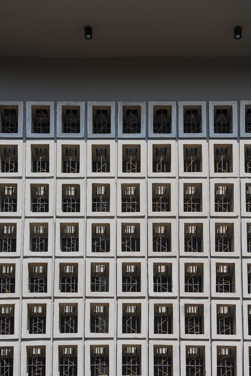 Grid facade of white concrete blocks with geometric metal screens in recessed openings
