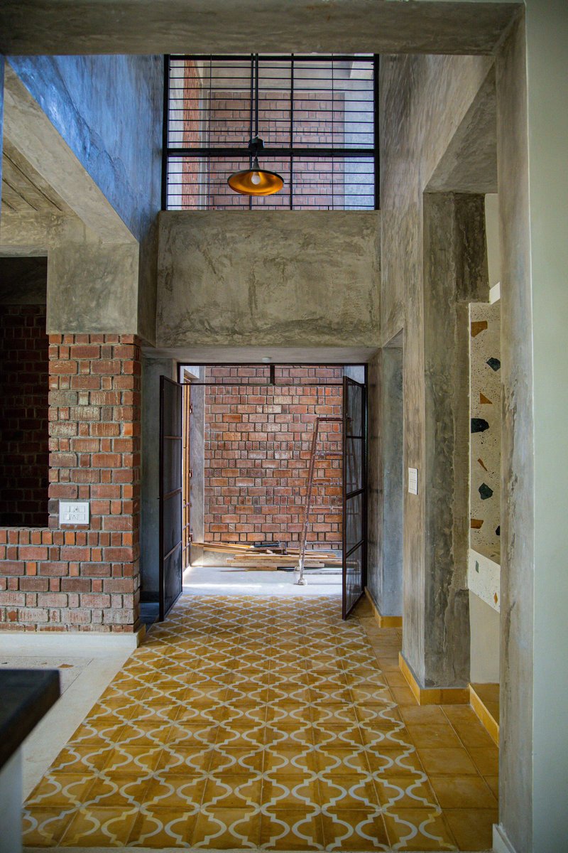 Double-height entryway with yellow patterned floor leading to brick wall and pendant light above