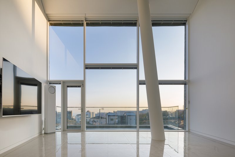 Double-height living space with floor-to-ceiling aluminum-framed windows overlooking distant rooftops at sunset