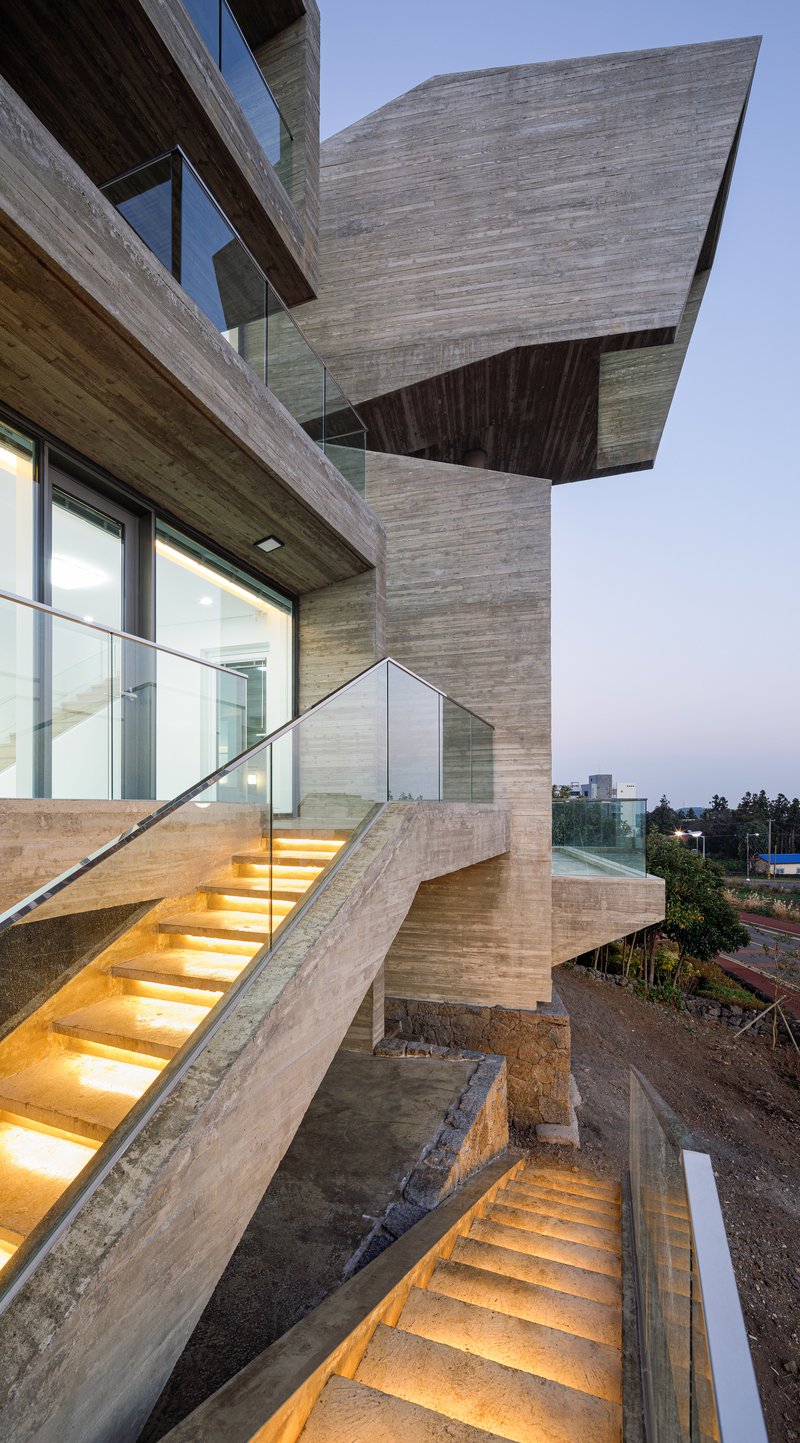 Exterior concrete staircase with integrated LED step lighting ascending between cantilevered volumes at twilight