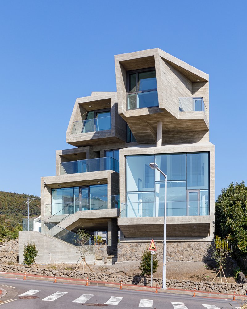 Stacked concrete volumes with floor-to-ceiling glass and cantilevered balconies facing a pedestrian crossing
