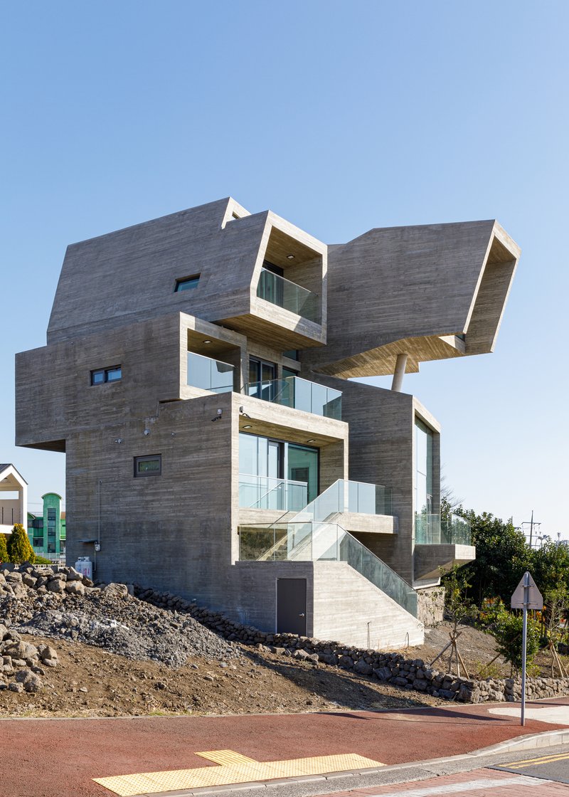 Side view showing cantilevered concrete boxes with glass railings on a sloped volcanic rock site