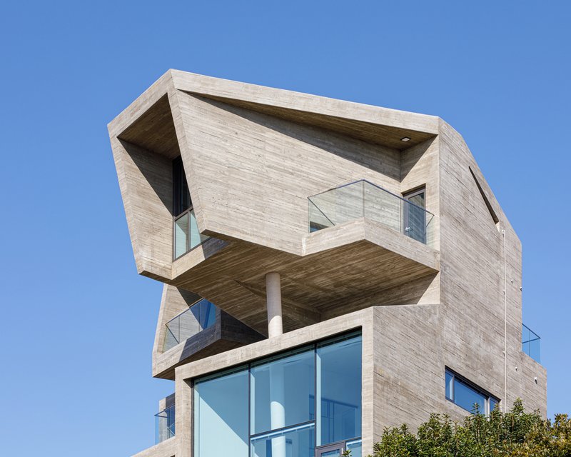 Cantilevered concrete volume with recessed balcony and glass railings under a clear blue sky