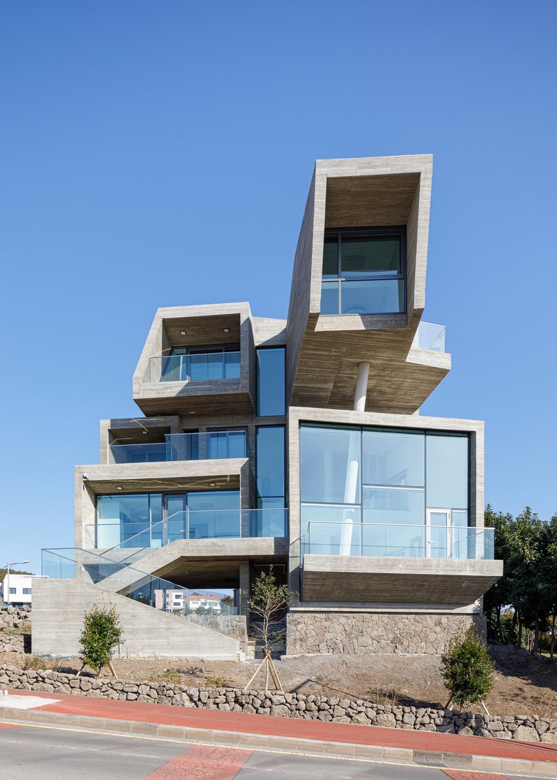Stacked concrete boxes with projecting balconies and floor-to-ceiling glazing on a sloped site