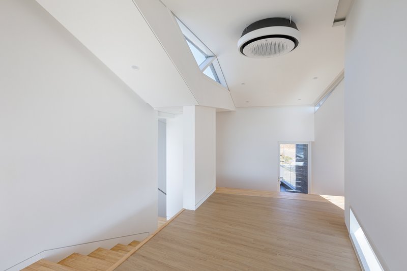 Open landing with timber flooring, white walls, cylindrical columns and clerestory windows below a sloped ceiling