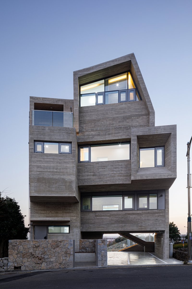 Street facade showing layered timber boxes with ribbon windows and stone base at dusk