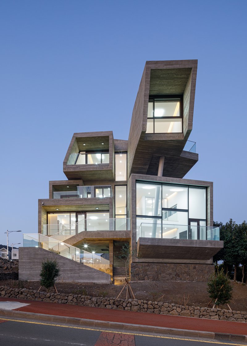 Stacked timber-clad volumes with floor-to-ceiling glazing overlooking the street at dusk