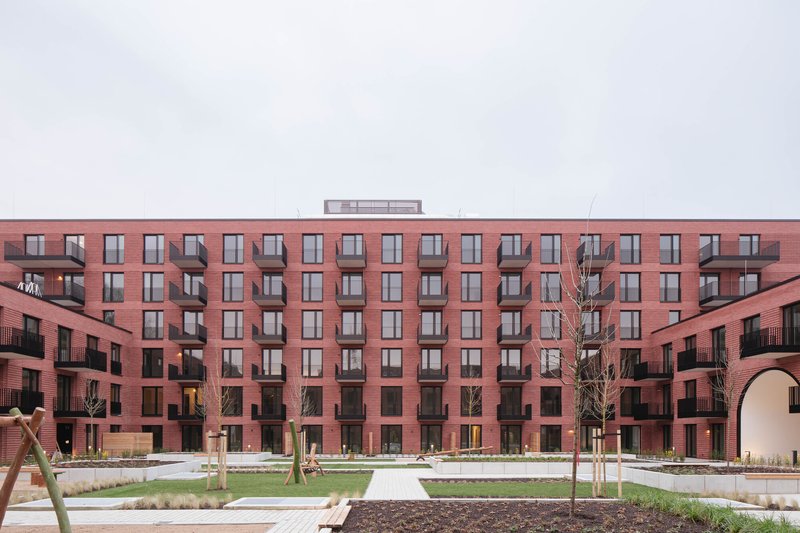 Courtyard view showing the symmetrical red brick facade with repetitive window pattern and rooftop pavilion under overcast sky