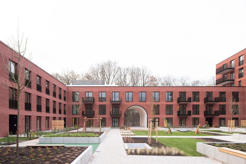 Central courtyard with landscaped beds and paved pathway framed by red brick residential blocks with a central archway
