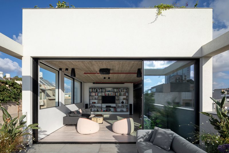 Sliding glass doors opening the living room to a rooftop terrace with plants and blue sky