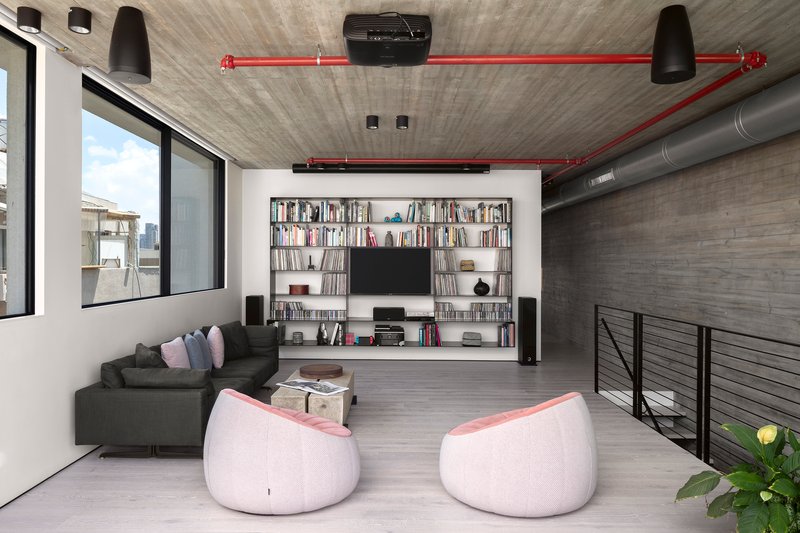 Living room with built-in bookshelf wall, exposed red fire suppression piping, and board-formed concrete ceiling