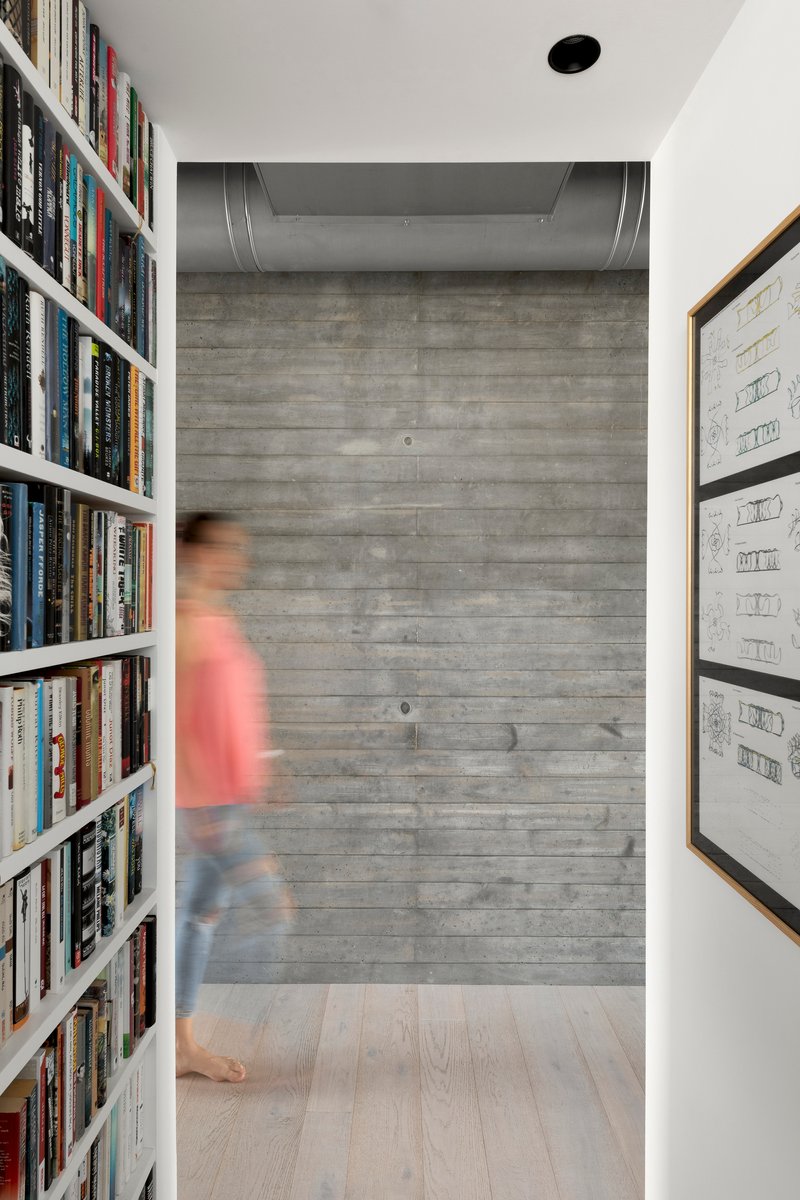 Hallway with board-formed concrete end wall and white bookshelves flanking a figure in motion blur