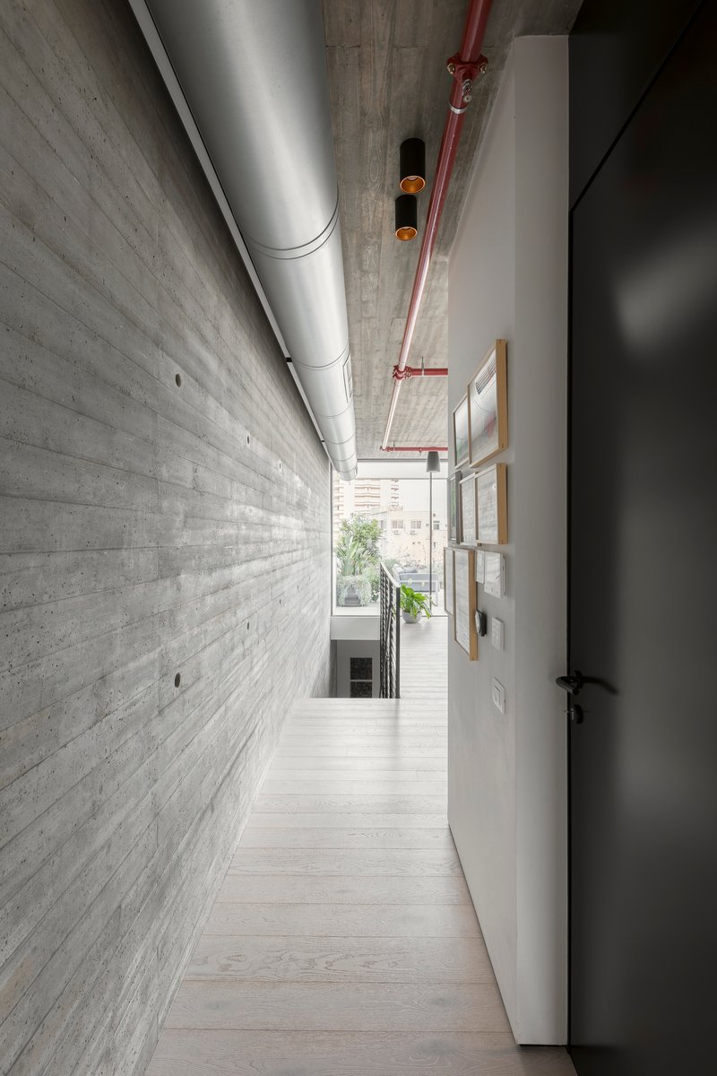 Narrow corridor with board-formed concrete wall alongside exposed HVAC ductwork and red fire suppression piping
