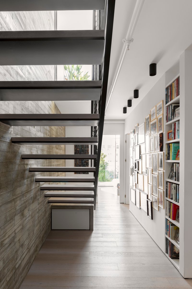 Open tread steel staircase beside board-formed concrete wall with built-in bookshelves and framed artworks