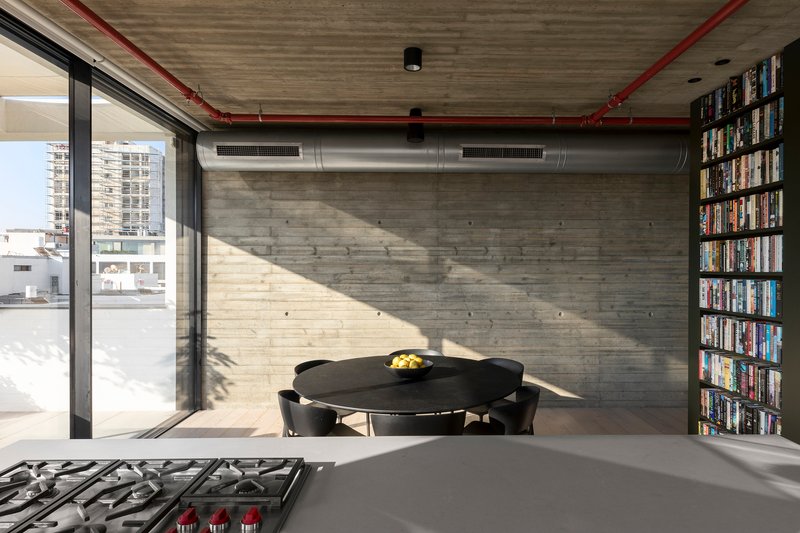 Dining area with exposed ductwork and red piping under board-formed concrete ceiling with bright sunlight streaming in