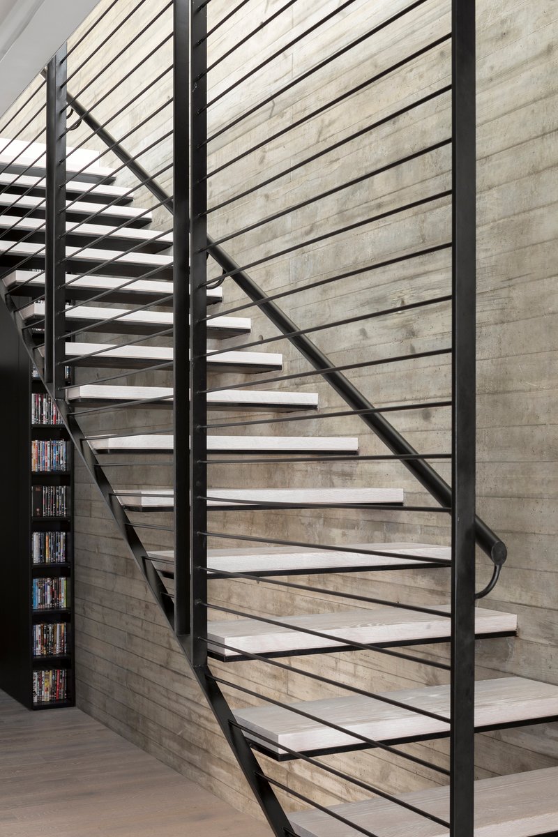 Close-up of cantilevered steel stair treads with horizontal cable railing against board-formed concrete wall