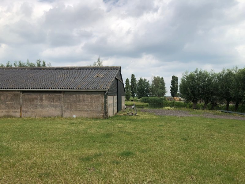Converted barn with concrete walls and metal roof extension across a grassy field under clouds