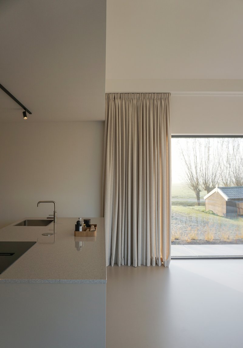 Kitchen island with integrated sink beneath linen curtains and a large window overlooking bare winter trees
