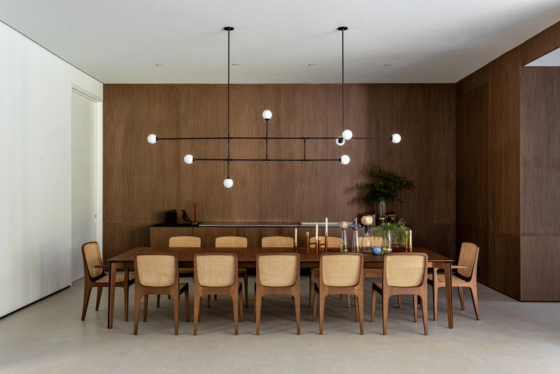 This architectural image showcases a modern dining room with a focus on natural materials and clean lines. The room features wood paneling, a large wooden dinin
