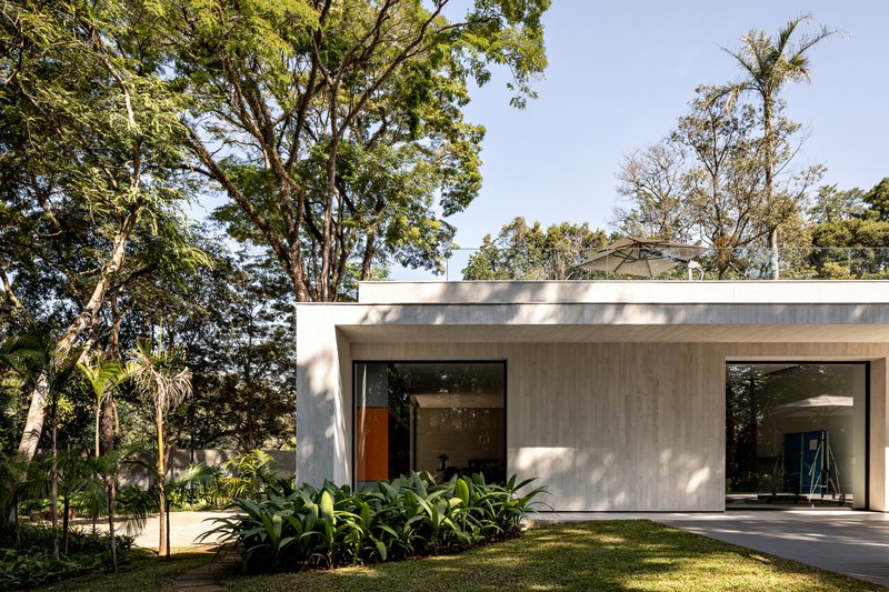 Single-story pavilion with board-formed concrete facade and large glazed openings set in lawn under mature trees